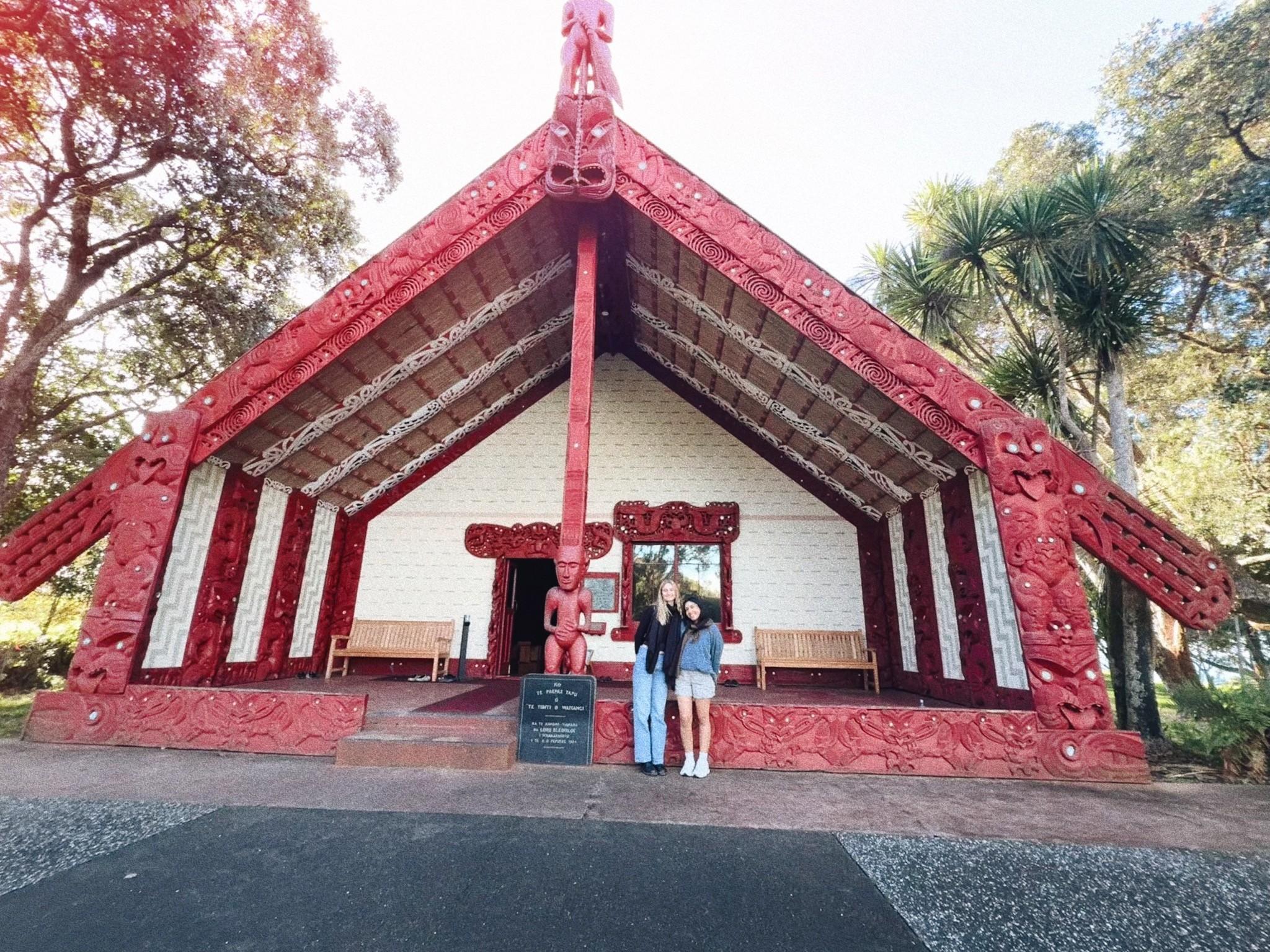 Two people standing in front of a building with sculptures of indigenous gods..