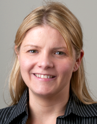 Smiling blonde woman headshot wearing black striped shirt on neutral gray background