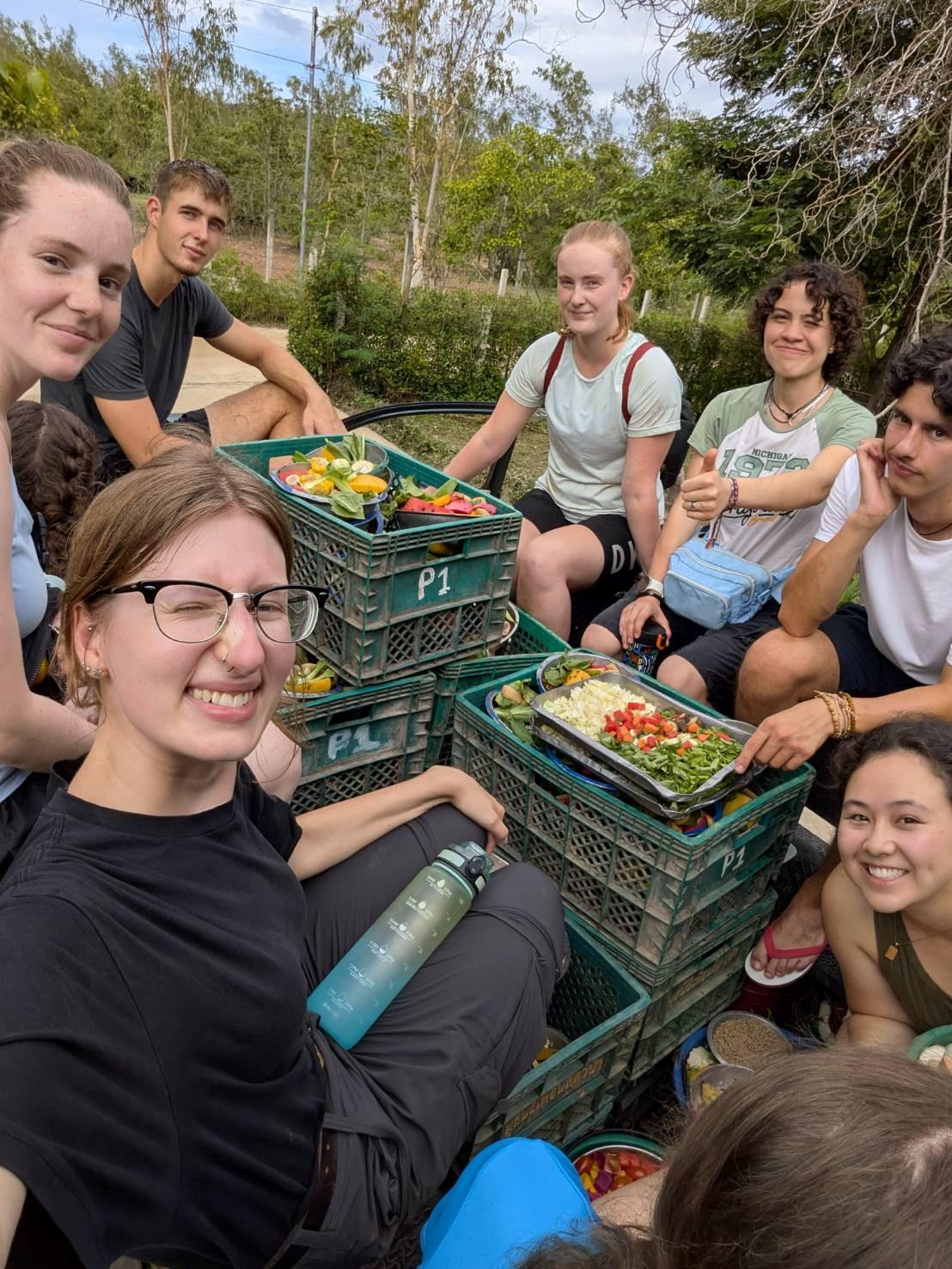 A group of people eating vegetables out of crates outside on a sunny day.