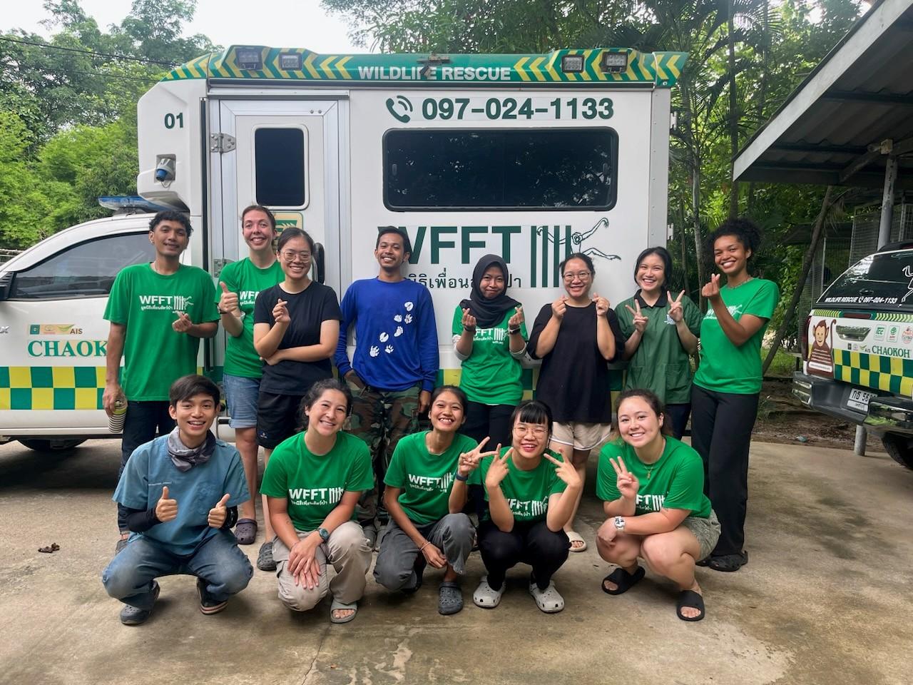 A group of people pose in front of a truck with the words painted on it, "wildlife rescue."