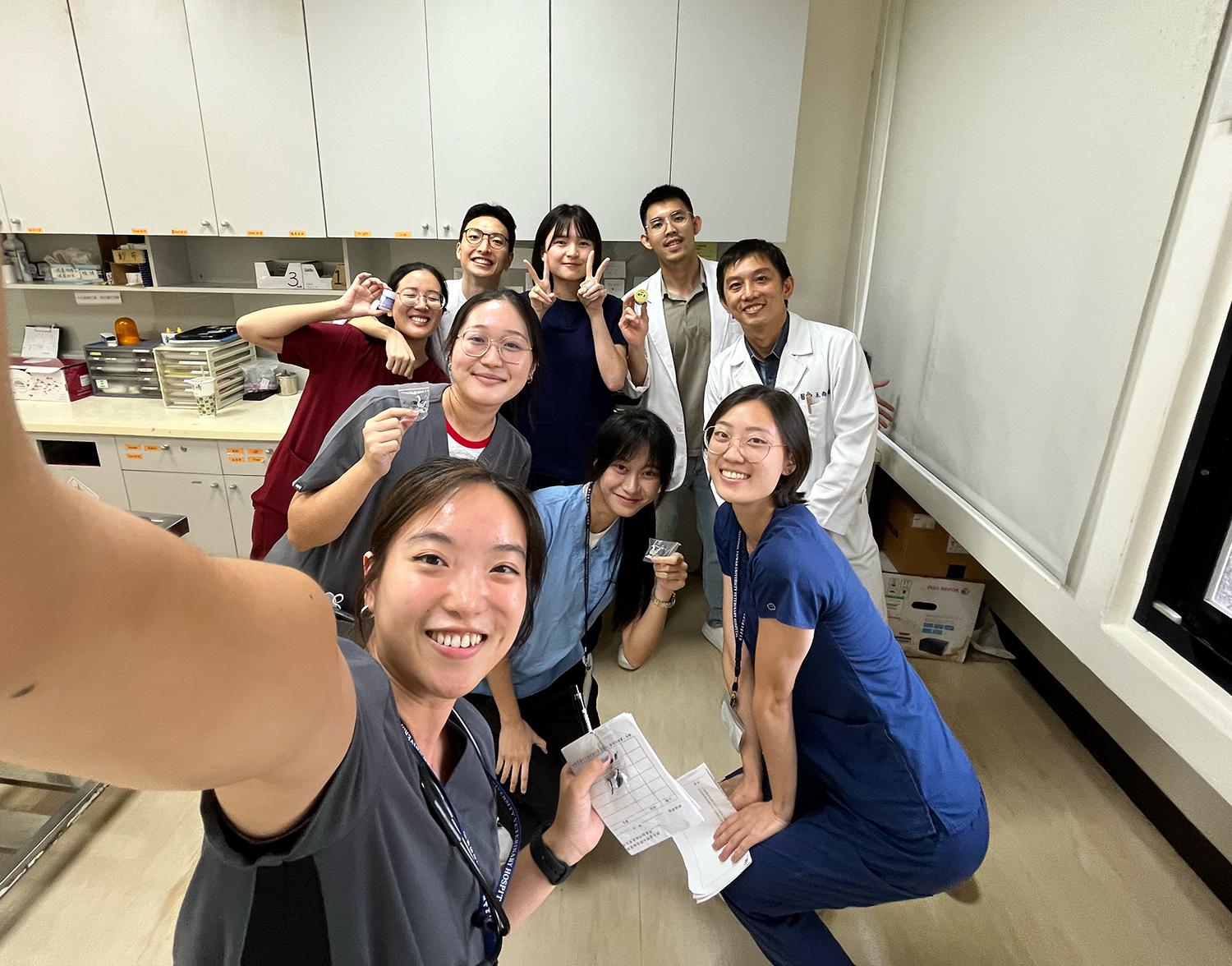 A group of 9 people posing for a photo in a clinic room.