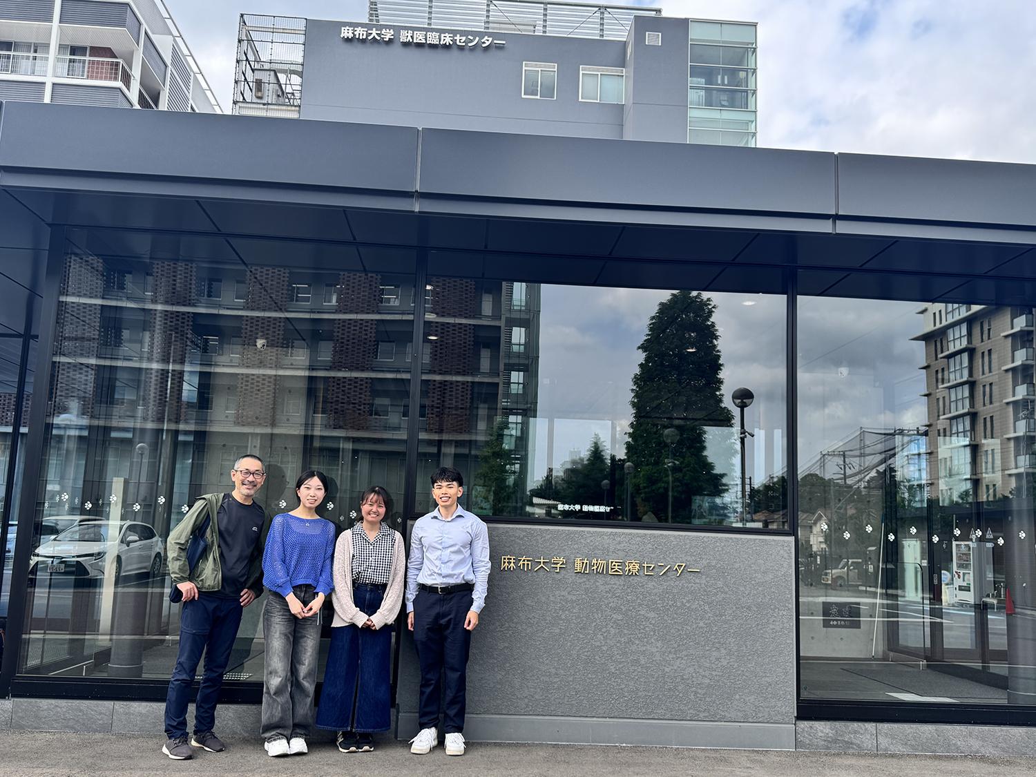 Four people standing in front of a city building with a sign that has Asian characters.