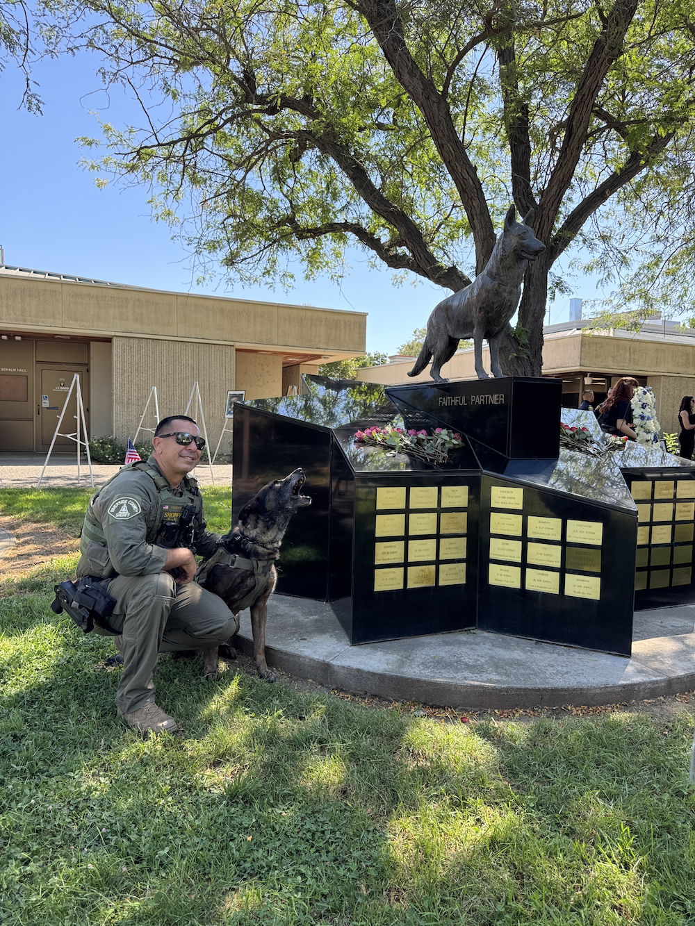 Uniformed man kneels with black dog beside black memorial topped by elephant statue