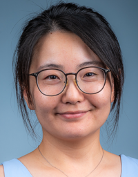 Smiling woman with round glasses, dark hair, light-blue top, studio photo portrait