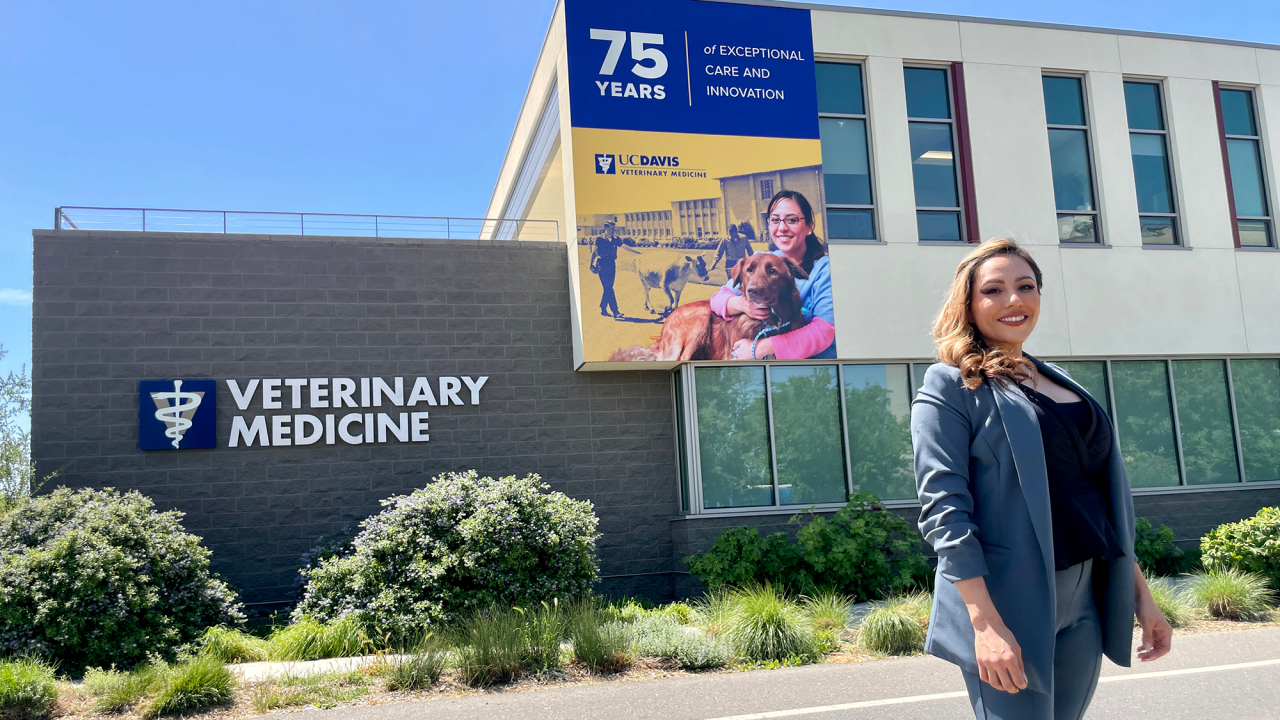 A woman standing in front of a building that displays a banner with her photo on it.