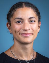 Headshot of smiling woman with pulled-back curly hair against blue background.