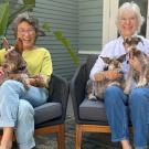 Two smiling people seated on a porch, each holding dogs.