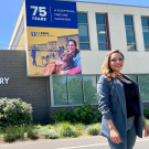 A woman standing in front of a building that displays a banner with her photo on it.