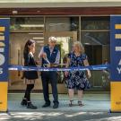 three people cutting ribbon in front of building