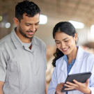 female veterinarian showing male worker information on portable computer while standing in poultry production facility